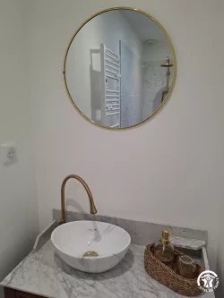 Miroir rond et robinet doré en salle de bain au Domaine des Hirondelles