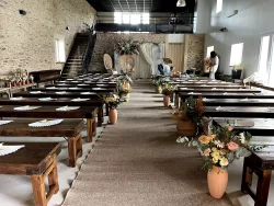 Cérémonie dans la grande salle, bancs décorés de fleurs au Domaine des Hirondelles